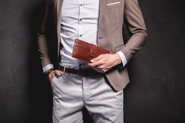 Retrato de moda de joven empresario guapo modelo hombre vestido con elegante traje marrón con accesorios