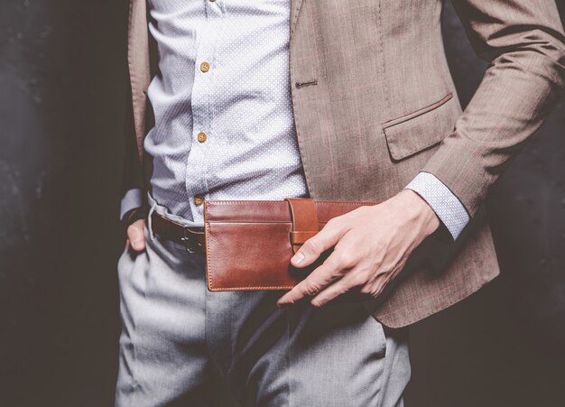 Retrato de moda de joven empresario guapo modelo hombre vestido con elegante traje marrón con accesorios