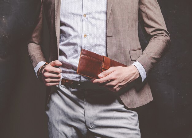 Retrato de moda de joven empresario guapo modelo hombre vestido con elegante traje marrón con accesorios