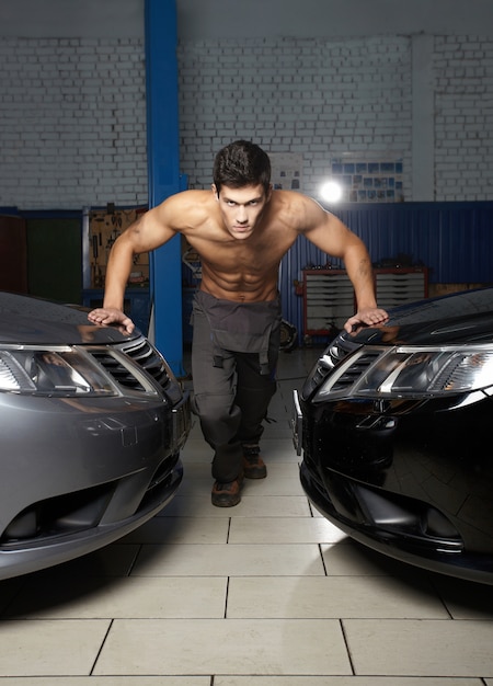 Retrato de moda de un joven musculoso de pie entre dos coches