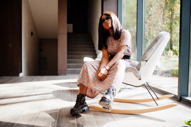 Retrato de moda de mujer afroamericana con botas largas y gafas de sol en el interior