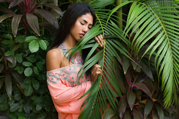 Retrato de moda de mujer asiática atractiva posando en jardín tropical. Lleva un vestido boho y accesorios elegantes.