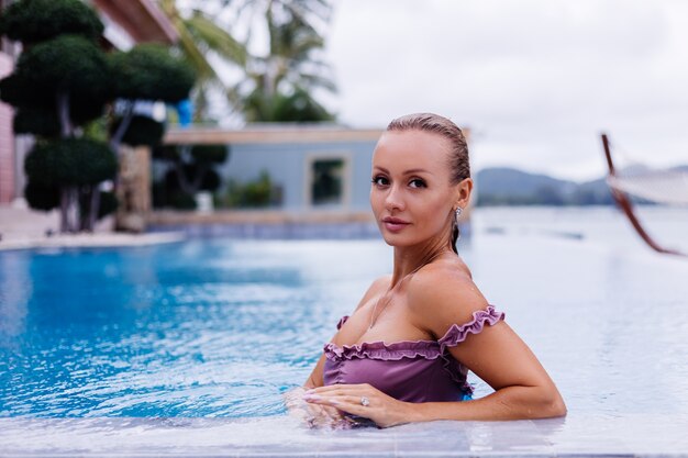 Retrato de moda de mujer caucásica en bikini en piscina azul de vacaciones en luz natural de día coudy