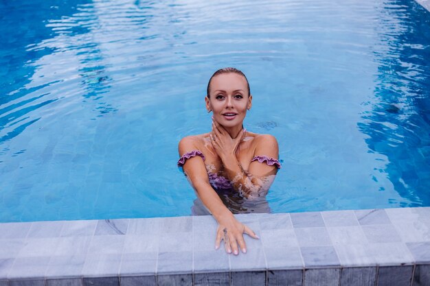 Retrato de moda de mujer caucásica en bikini en piscina azul de vacaciones en luz natural de día coudy