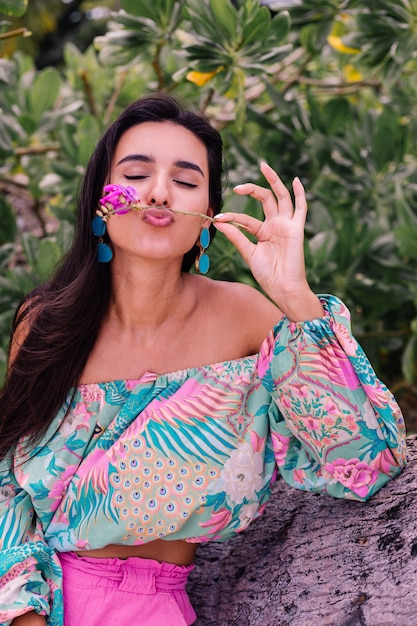 Foto gratuita retrato de moda de mujer elegante en top de manga larga con estampado de colores y pantalones cortos de color rosa en la playa, fondo tropical.