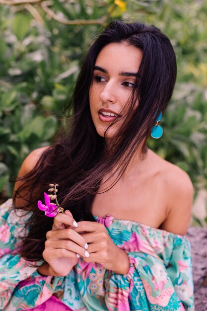 Retrato de moda de mujer elegante en top de manga larga con estampado de colores y pantalones cortos de color rosa en la playa, fondo tropical.