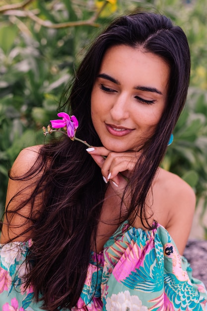 Retrato de moda de mujer elegante en top de manga larga con estampado de colores y pantalones cortos de color rosa en la playa, fondo tropical.