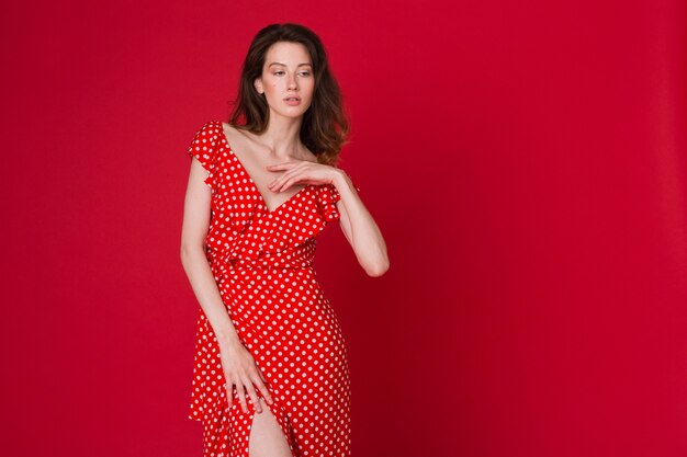 Retrato de moda de mujer joven sonriente atractiva en vestido rojo punteado en estudio rojo