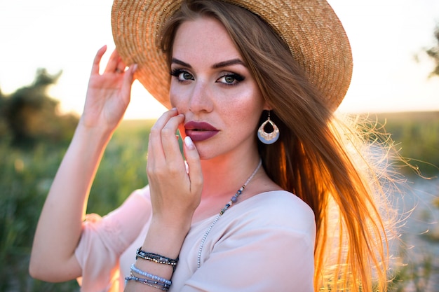 Retrato de moda de mujer rubia sensual, maquillaje brillante, joyería de moda, estilo boho, efecto de película, posando al aire libre de cerca.