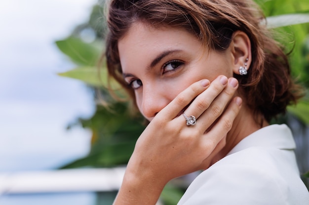 Retrato de moda de mujer en villa de lujo tropical vistiendo elegante blazer blanco y joyas sobre hojas tropicales