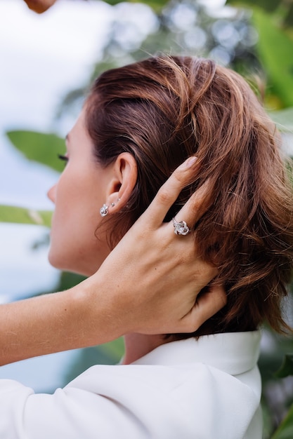 Retrato de moda de mujer en villa de lujo tropical vistiendo elegante blazer blanco y joyas sobre hojas tropicales