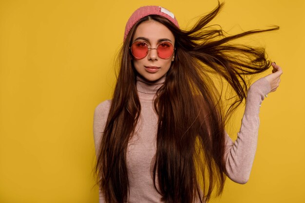 Retrato de moda de niña vistosa con cabello volador con gorra y gafas rosas redondas