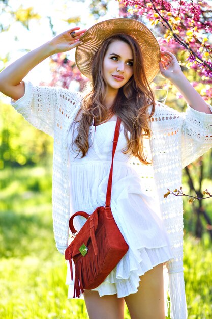 Retrato de moda de primavera de modelo elegante posando en el parque floreciente de Sakura, disfruta de un día cálido y soleado