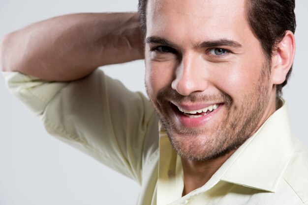 Retrato de moda de primer plano de hombre sonriente en camisa amarilla con poses de mano cerca de la cara