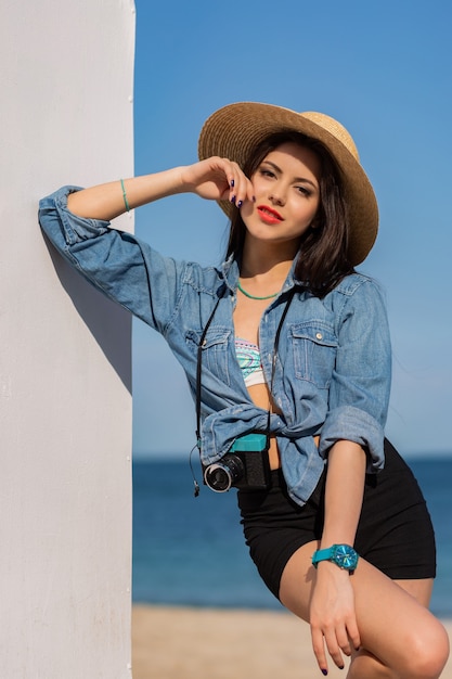 Retrato de moda de verano al aire libre de hermosa mujer con cuerpo bronceado, labios rojos llenos y piernas largas y fuertes posando en la playa tropical soleada.