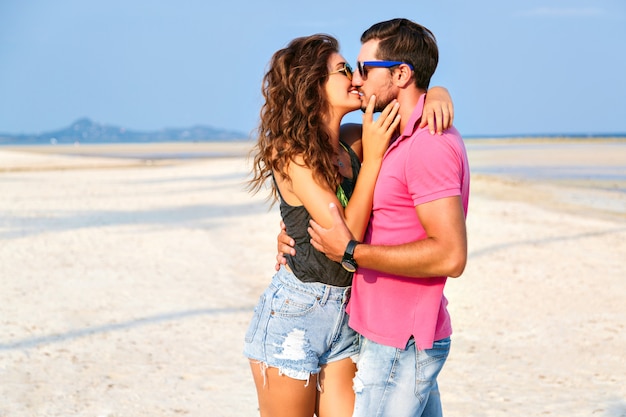 Foto gratuita retrato de moda de verano de joven pareja de hipsters muy elegantes enamorados abrazos y posando en la increíble playa de la isla, divirtiéndose solo, vistiendo ropa casual brillante y gafas de sol.