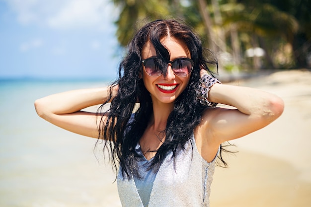 Retrato de moda de verano lindo de mujer morena de belleza divirtiéndose en la playa, bailando y sonriendo