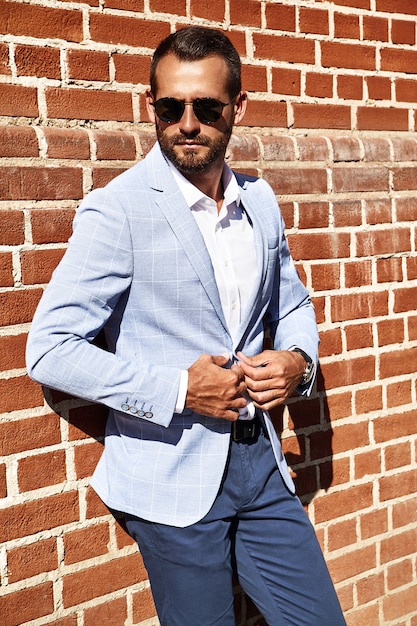 El retrato del modelo atractivo atractivo del hombre de negocios de la moda se vistió en el traje azul elegante que presentaba cerca de la pared de ladrillo en el fondo de la calle. Metrosexual