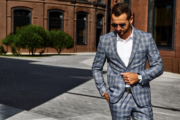 Foto gratuita el retrato del modelo atractivo atractivo del hombre de negocios de la moda se vistió en el traje a cuadros elegante que presentaba en fondo de la calle. metrosexual