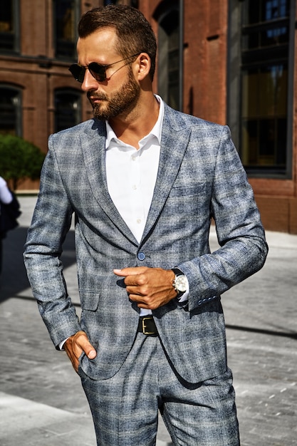 El retrato del modelo atractivo atractivo del hombre de negocios de la moda se vistió en el traje a cuadros elegante que presentaba en fondo de la calle. Metrosexual