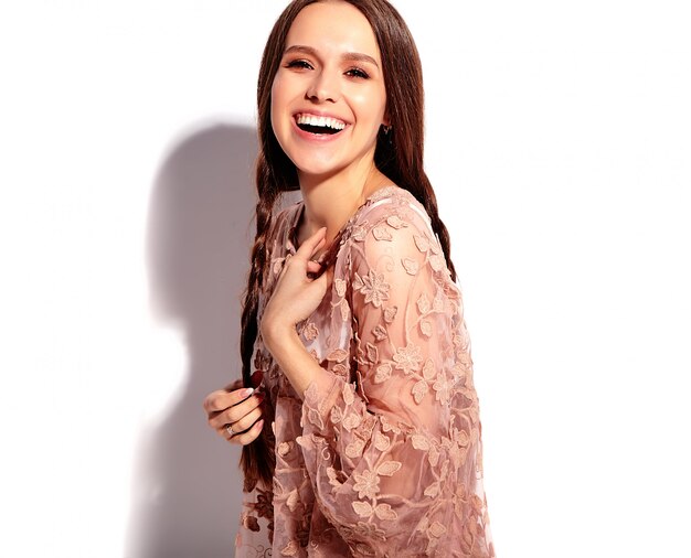 Retrato del modelo caucásico sonriente de la mujer morena hermosa con las coletas dobles en la ropa elegante del verano rosado brillante aislada en el fondo blanco.