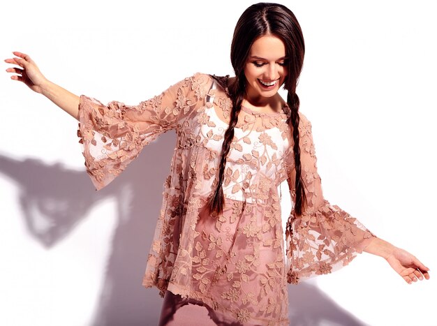 Retrato del modelo caucásico sonriente de la mujer morena hermosa con las coletas dobles en la ropa elegante del verano rosado brillante aislada en el fondo blanco.