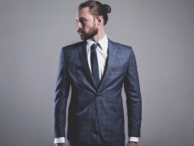 Retrato de modelo de empresario de moda guapo vestido con elegante traje azul con gafas posando en gris