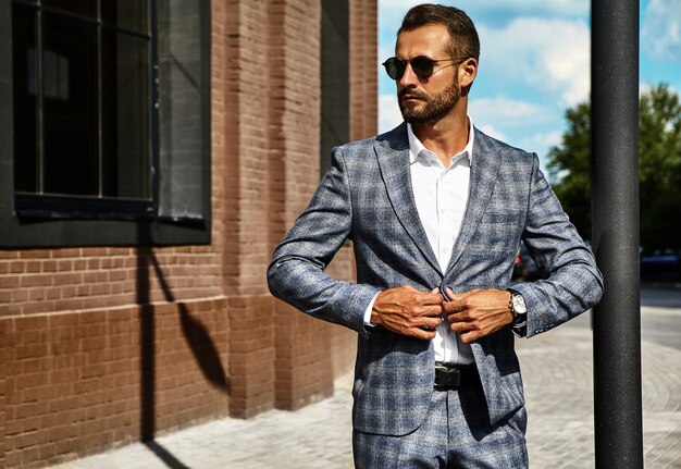 Retrato del modelo de empresario de moda guapo vestido con elegante traje a cuadros posando en la calle