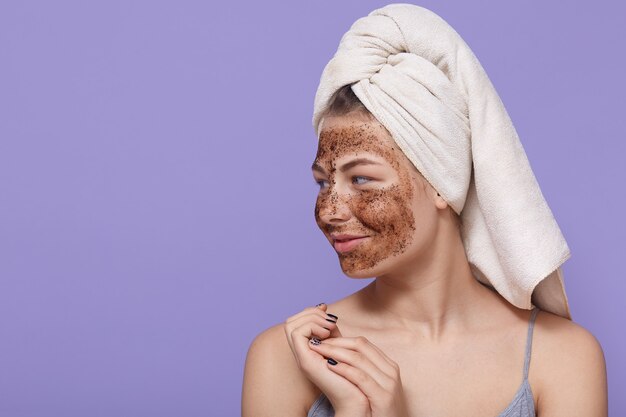 Retrato de modelo femenino aplica máscara de chocolate en la cara, tiene expresión positiva, mira a un lado