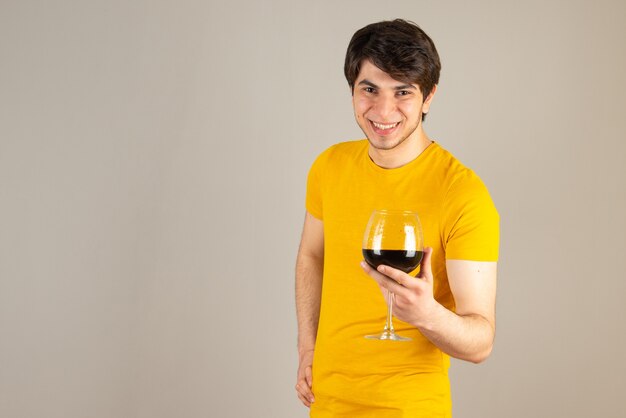 Retrato de un modelo de hombre sonriente en camisa amarilla de pie y sosteniendo una copa de vino.