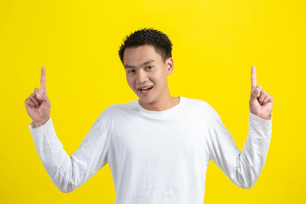 Retrato de modelo masculino apuntando con el dedo hacia arriba y sonriendo en la pared amarilla