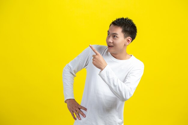 Retrato de modelo masculino apuntando con el dedo hacia arriba y sonriendo en la pared amarilla