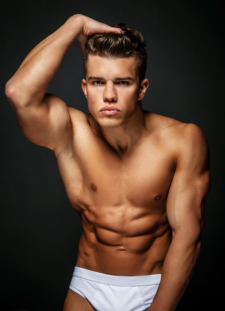 Retrato de modelo masculino impresionante con cuerpo musculoso desnudo. Aislado sobre fondo gris oscuro.