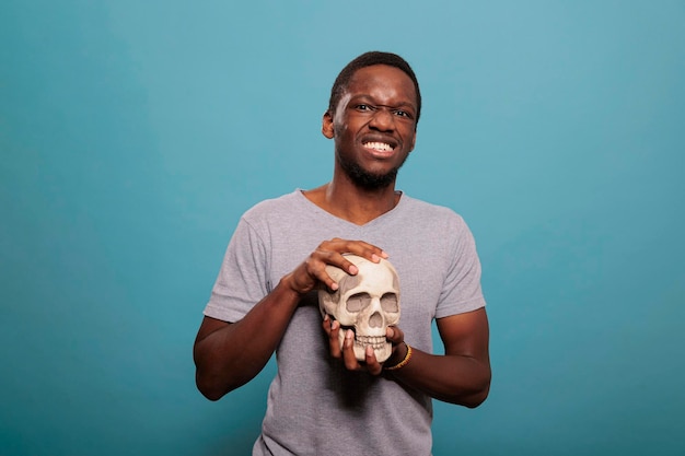 Retrato de un modelo masculino que sostiene el cráneo del esqueleto humano para estudiar la enfermedad cerebral científica genética, la anatomía y la educación biológica. Tema anatómico para descubrir el conocimiento de la ciencia.