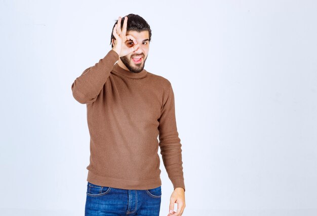 Retrato de modelo masculino en suéter marrón de pie sobre una pared blanca.