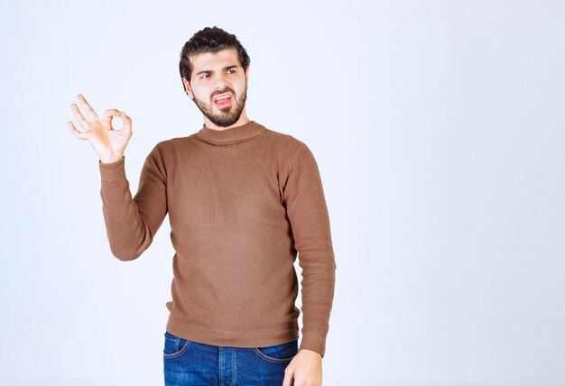 Retrato de modelo masculino en suéter marrón de pie sobre una pared blanca.