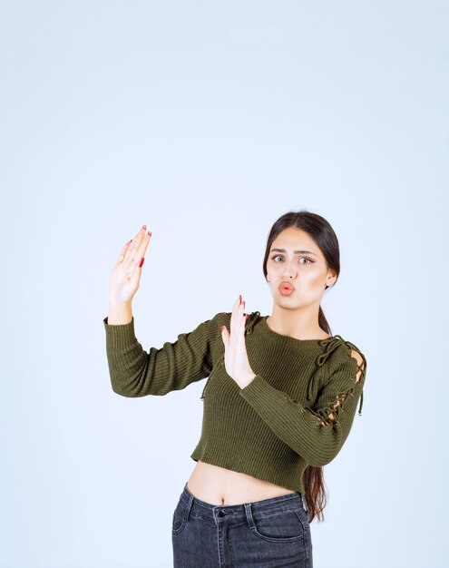 Retrato de un modelo de mujer joven empujando algo en el lado sobre la pared blanca.