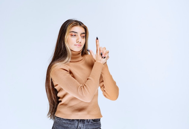 Retrato de un modelo de mujer joven en suéter marrón levantando los dedos como una pistola.