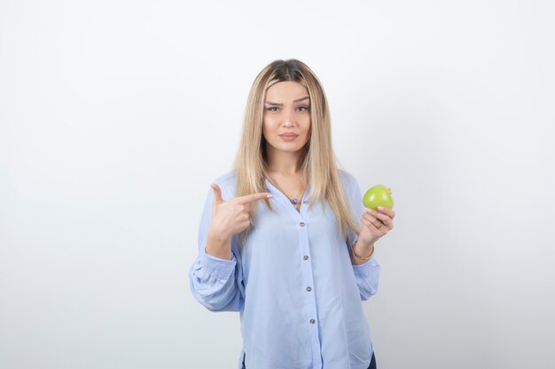 retrato de un modelo de niña bonita de pie y apuntando a una manzana verde fresca.