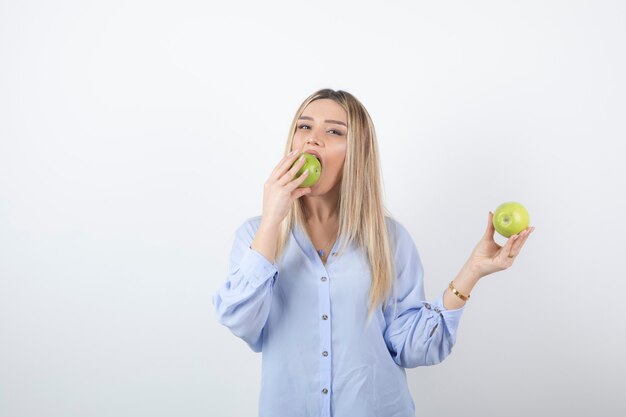 retrato de un modelo de niña bonita de pie y comiendo una manzana verde fresca.