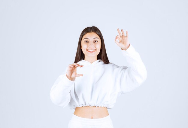 Retrato de un modelo de niña feliz con una tarjeta que muestra el gesto ok.