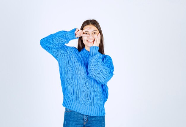 Retrato de un modelo de niña sonriente que muestra el signo de la victoria cerca del ojo.