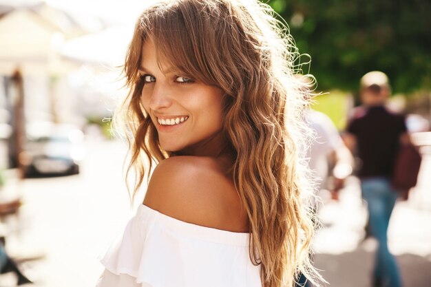 Retrato del modelo rubio sonriente lindo hermoso del adolescente sin maquillaje en el vestido blanco del inconformista del verano que presenta en el fondo de la calle. Giro de vuelta