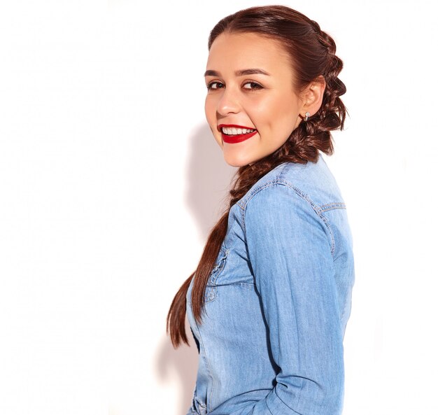 Retrato del modelo sonriente feliz joven de la mujer con maquillaje brillante y labios rojos con dos coletas en la ropa de los tejanos del verano aislada.