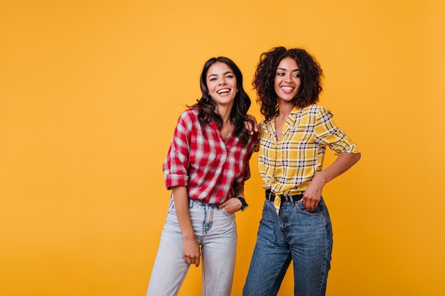 Retrato de modelos alegres con rizos en camisas a cuadros. Las chicas bronceadas se divierten.