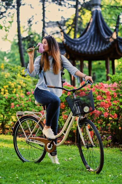 Retrato de morena con bicicleta de ciudad cerca del pabellón chino tradicional en un parque.