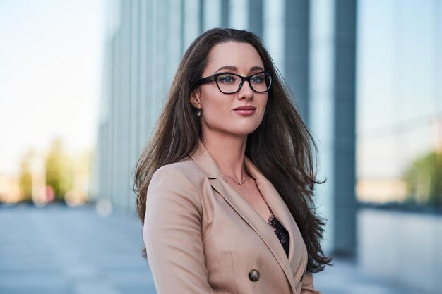 Retrato de una morena inteligente con gafas en la calle con una interesante arquitectura de fondo.