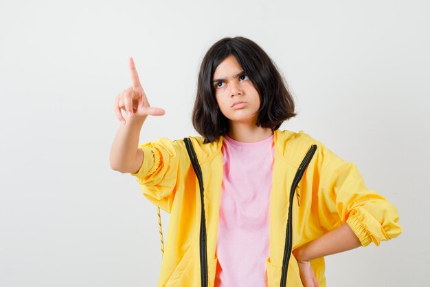 Retrato de muchacha adolescente apuntando hacia arriba en camiseta, chaqueta y mirando seriamente vista frontal