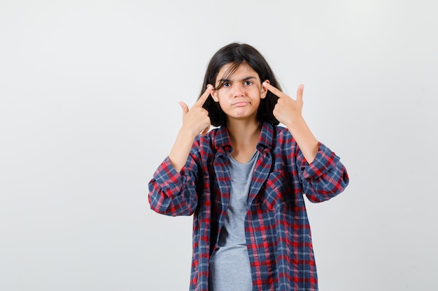 Retrato de muchacha adolescente apuntando a sus ojos en ropa casual y mirando triste vista frontal