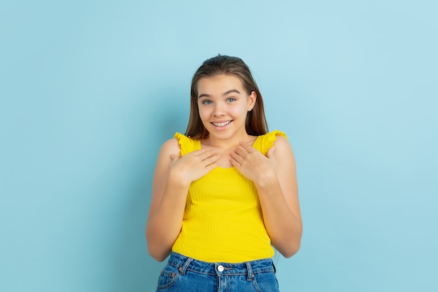 Retrato de la muchacha adolescente caucásica aislado sobre fondo azul. Hermosa modelo en ropa casual de color amarillo.